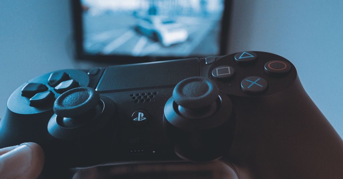 Hand holding a gaming controller in front of a blurred backlit screen